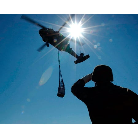 Soldier observes a UH-60 Blackhawk as it prepares to drop slingloaded prepackaged food Poster Print by Stocktrek