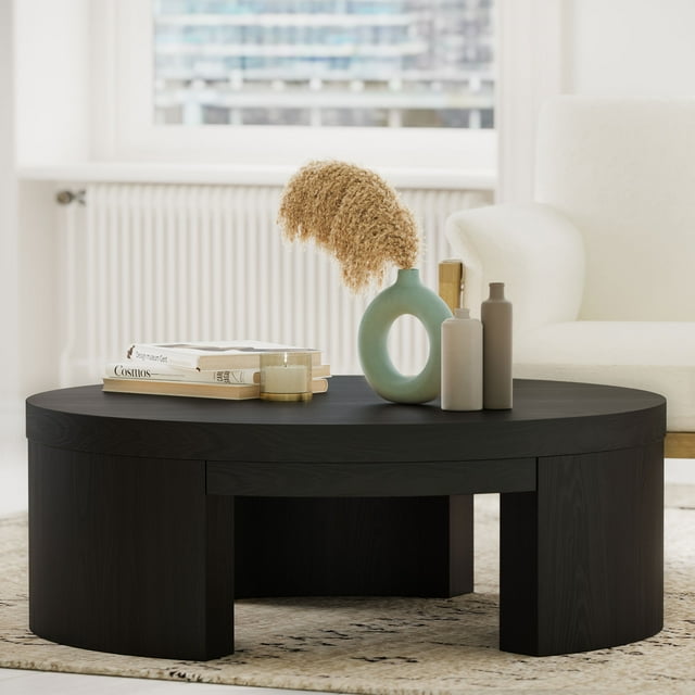 Modern round coffee table in rich black finish by Drew Barrymore, styled with minimalist vases and books on a textured rug.