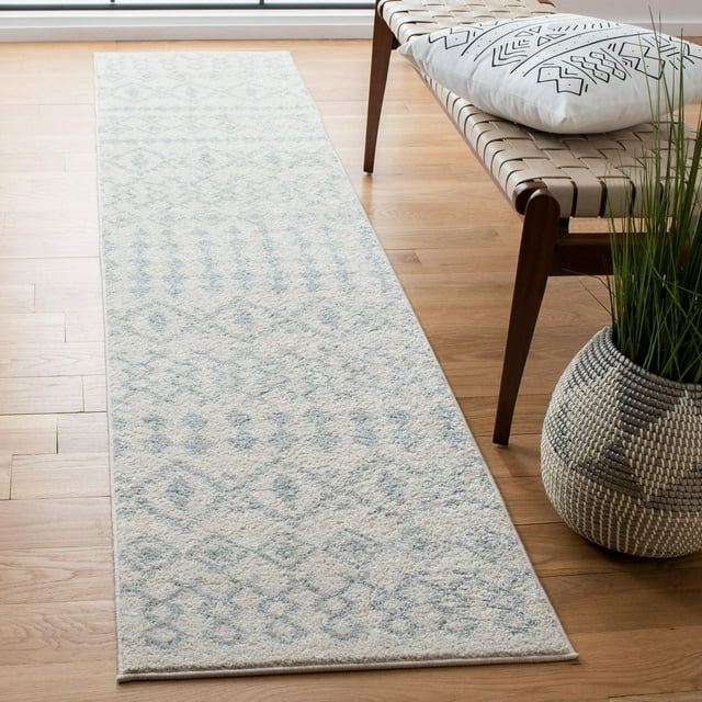 SAFAVIEH Tulum Herbert distressed southwestern area rug runner in light blue and beige on hardwood floor beside woven bench with geometric pillow and potted plant.
