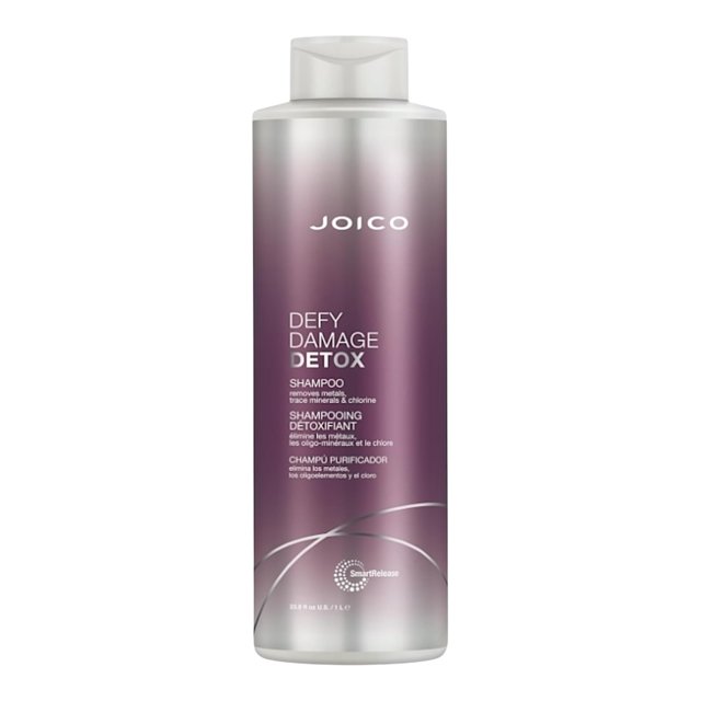 Joico Defy Damage Shampooing Détox 33,8 Oz dans une Bouteille Cylindrique avec un Motif Dégradé Violet et un Texte Blanc. Ce Shampooing Végétalien Sécuritaire pour la Couleur Est Formulé avec du Charbon Activé et un Chélateur Biosourcé pour Éliminer les Résidus d'Eau Dure, les Traces de Minéraux et l'Accumulation de Produits Tout en Préservant l'Humidité. la Bouteille Affiche de Façon Prééminente l'Image de Marque et les Détails du Produit.