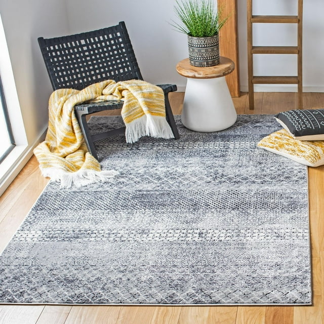 Distressed southwestern area rug in gray tones with subtle geometric designs, styled with a black woven chair draped by a yellow and white throw, wooden stool holding a potted plant, and decorative pillows on light wood flooring.