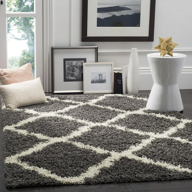 Safavieh Dallas Logan gray shag area rug featuring a white geometric diamond pattern, styled with pillows and framed art in a contemporary room.