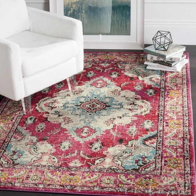 Safavieh Monaco Toria Traditional Area Rug with a bohemian Persian design in cream, blue, and pink tones, made of durable polypropylene, placed under a white armchair with clear legs beside stacked art books topped with a geometric metal decor on dark hardwood flooring, ideal for vibrant accent in living rooms.