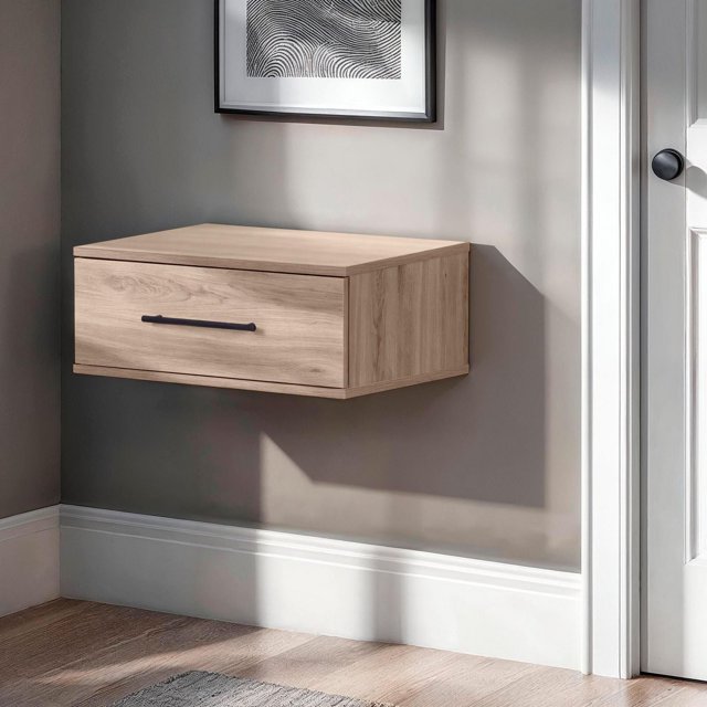 Southshore Primo floating nightstand in light wood with one drawer and black handle, mounted on a gray wall near a white door.