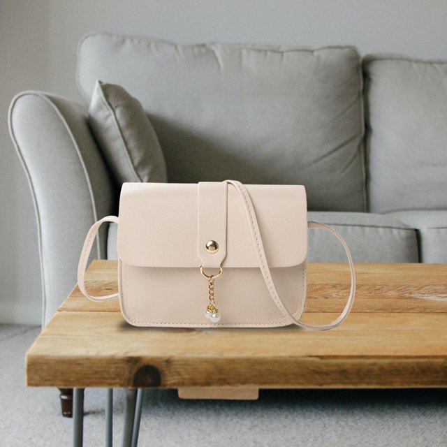 bolso bandolera para mujer, bolso de hombro elegante, ligero, versátil, bolso de mano tipo bandolera para playa, oficina, viajes, festivales, regalo beige salvador bolsos cruzados Beige Salvador Dali bandolera frontal sobre mesa de madera; forma rectangular con solapa y correa larga en tela, cierre con botón dorado y cadena con colgante tipo perla; textura lisa, medidas 17 x 12.5 x 5 cm. Fondo: sofá gris desenfocado. También suele usarse para llevar esenciales de viaje.