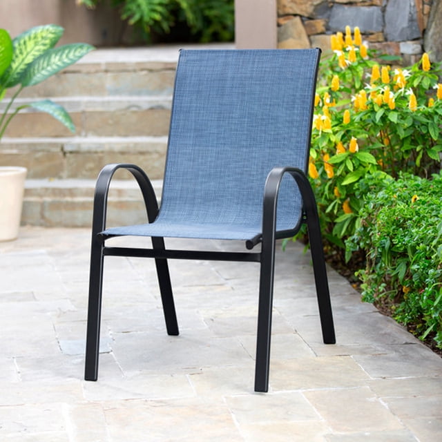 silla apilable sling - denim silla apilable con funda de tela denim azul y estructura metálica negra, vista frontal 3/4; asiento y respaldo en tejido sling estirado, reposabrazos curvados y patas inclinadas, colocada en patio empedrado junto a plantas y flores, apta para uso exterior y fácil limpieza con paño húmedo; a menudo se usa en terrazas y áreas de descanso al aire libre.