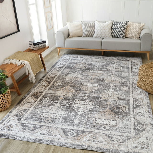 Distressed vintage-style indoor area rug in brown and beige tones featuring geometric patterns, placed under a light gray sofa with patterned cushions in a bright living room.