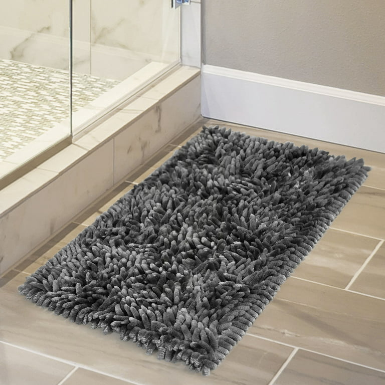 A cream fringe bath rug sits atop gray marble hexagon floor tiles in front  of a roll top freestanding …