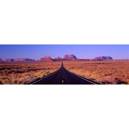 This is Route 163 that runs through the Navajo Indian Reservation The road runs up the middle and gets smaller into infinity The red rocks of Monument Valley are in the background The scrub plants (Best Way To Get To Monument Valley)