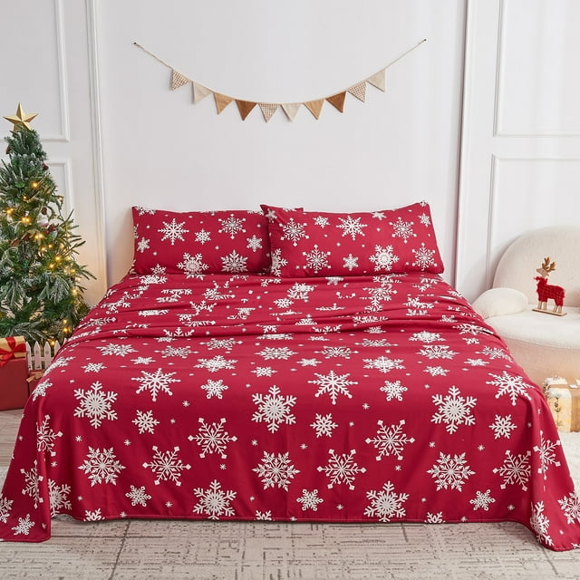 Gogreen 4PC Queen Sheet Set with a deep pocket fit of 16 inches, featuring a red background with white Christmas snowflake patterns. The set includes a flat sheet, fitted sheet, and two pillowcases, made from breathable, fade-resistant 90GSM microfiber for year-round comfort. Displayed on a queen-sized bed in a holiday-themed room with a Christmas tree and festive decor.
