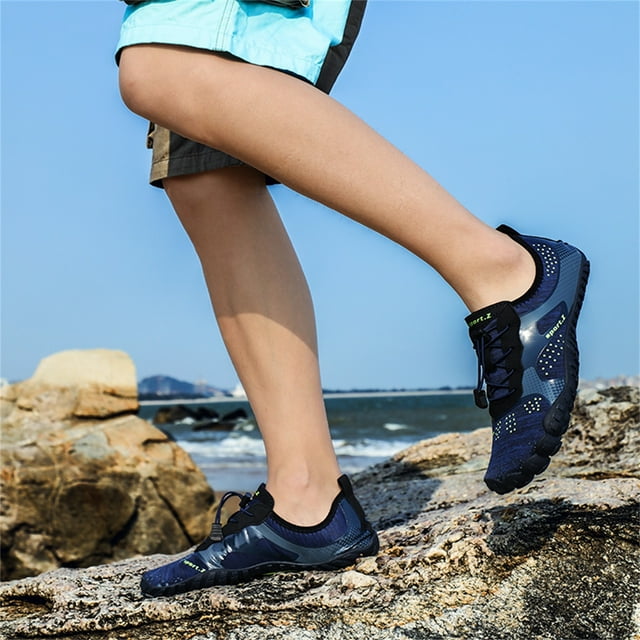 pareja zapatos de playa zapatos de natación zapatos de agua descalzo zapatos de agua de secado rápido wmkox8yii 123q1278 Azul oscuro — 3/4 lateral de zapatos de agua de corte bajo con empeine de tejido elástico, suela PVC antideslizante texturizada y plantilla EVA; slip-on con cordón visible; modelo caminando sobre rocas en la costa; calzado acuático adecuado para natación, senderismo ligero y viajes, y que suele usarse también para gimnasio o yoga.