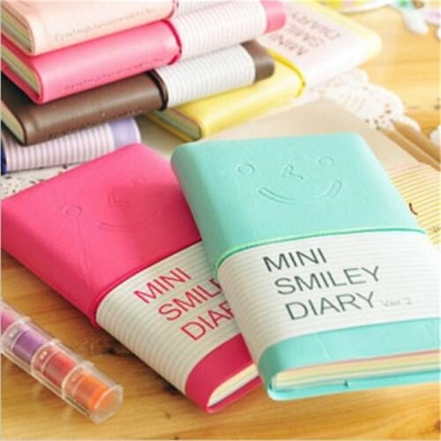 fiudx libreta de bolsillo, diseño pequeño de cuero con estampado de caritas felices, juego de 5 piezas 13 x 8 x 1,5 cm; vista 3/4 frontal de agendas turquesa y rosa con banda elástica blanca que dice "MINI SMILEY DIARY", cubiertas con carita en relieve y páginas visibles sobre escritorio de madera; también adecuada como libreta de notas portátil para listas rápidas en oficina o hogar.