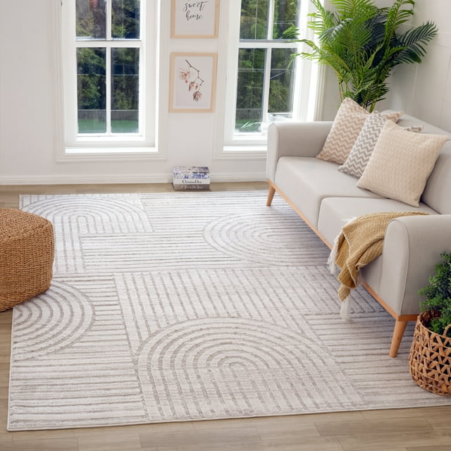 Grey modern indoor area rug featuring geometric arches and lines pattern in a bright living room with light gray sofa, decorative pillows, woven pouf, and green plants.