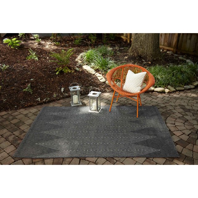 dark gray ECARPET Raven contemporary area rug with subtle zigzag pattern displayed on outdoor stone patio under an orange woven chair and two silver lanterns