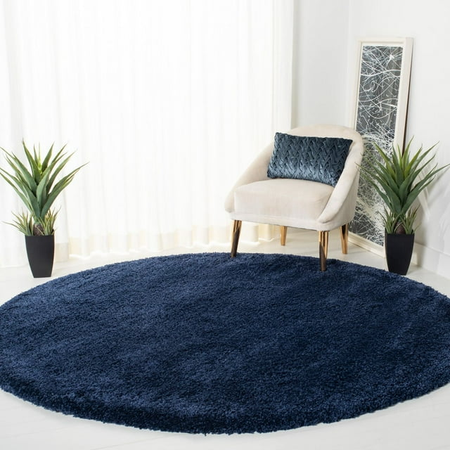 Round navy blue Safavieh Milan Harlow solid shag area rug displayed in a modern living space with beige chair and green plants.