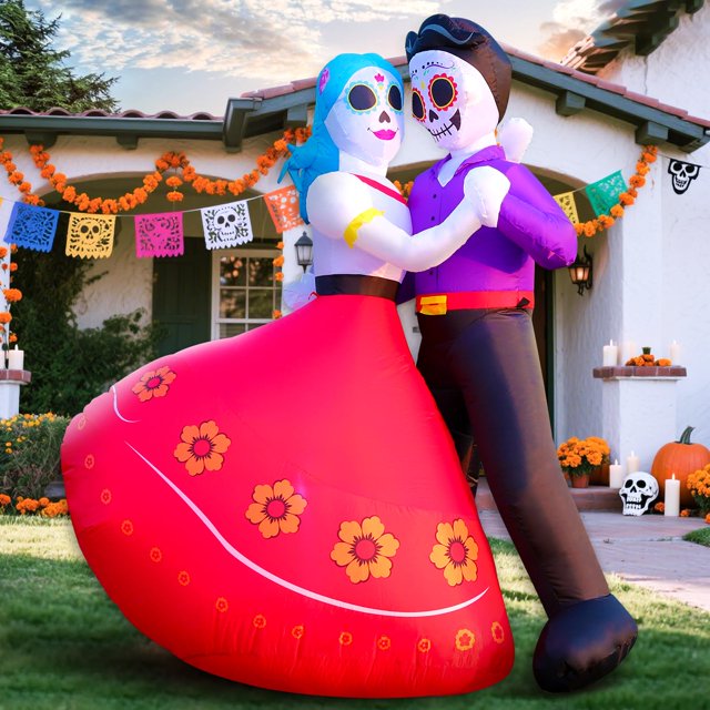 pareja hinchable domkom para día de los muertos, 183 cm, con led — pareja de esqueletos Catrina y Catrín en pose de baile, vista frontal 3/4 en jardín; falda roja con flores impresas y blusa azul, traje morado y pantalón negro en el compañero, calaveras con detalles coloridos y LEDs integrados que iluminan el atuendo, fondo con papel picado, velas y ofrendas en césped; adecuada para decorar entrada o altar durante la celebración.