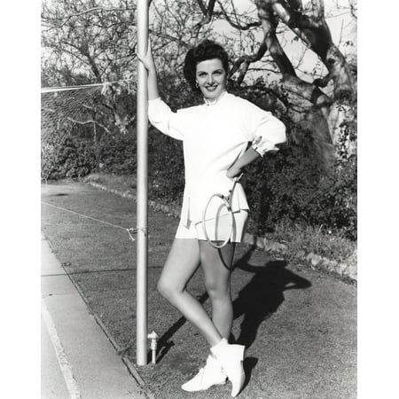 Jane Russell Posed in White Long Sleeve Shirt and Short Pants with Hands Holding a Tennis Racquet while Legs Crossed in White Rubber Shoes Photo
