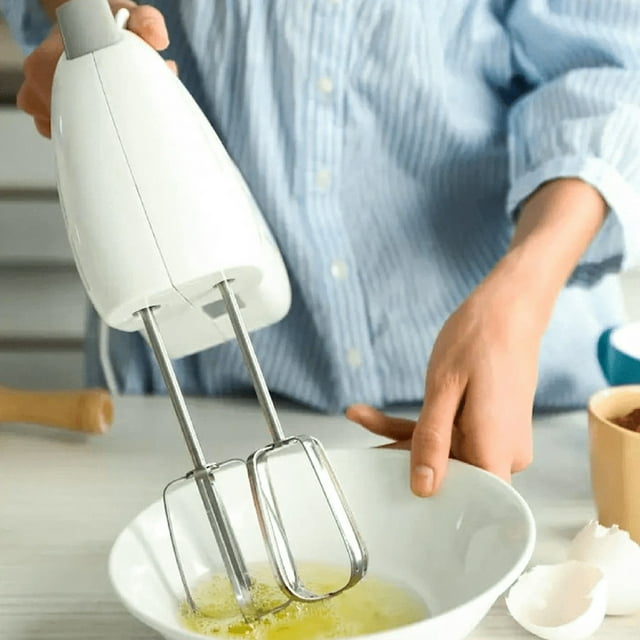 2Pcs Mixing Heads, Hand Mixer Beaters Attachments made of stainless steel, shown attached to a handheld electric mixer. The beaters feature a classic whisk-like design with multiple thin, curved wires, ideal for mixing batters, whipping cream, or beating eggs. A person is using the mixer to blend ingredients in a white bowl, with eggshells and other kitchen items visible in the background.