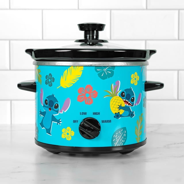 uncanny brands cocina lenta de 2 cuartos de galón disney lilo & stitch — Vista frontal centrada de olla compacta turquesa con ilustraciones de Lilo y Stitch, flores y hojas tropicales; perilla frontal marcada Off/Low/Warm/High, asas negras y tapa de vidrio, inserto cerámico extraíble; ideal para preparar sopas, guisos y calentar salsas.