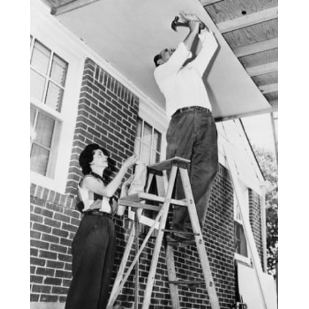 Low angle view of a mid adult man fixing plywood on a porch with a mid adult woman helping him Stretched Canvas -  (24 x