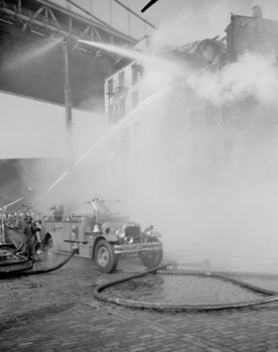 Firefighter pouring water on burning building near fire engine Poster