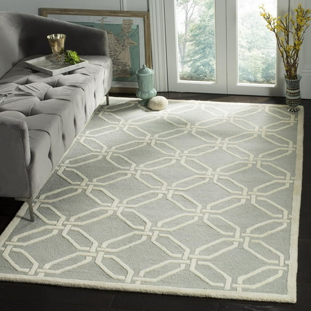 Safavieh Cambridge Kierra light gray area rug with off-white geometric chain-link design under a tufted gray sofa.