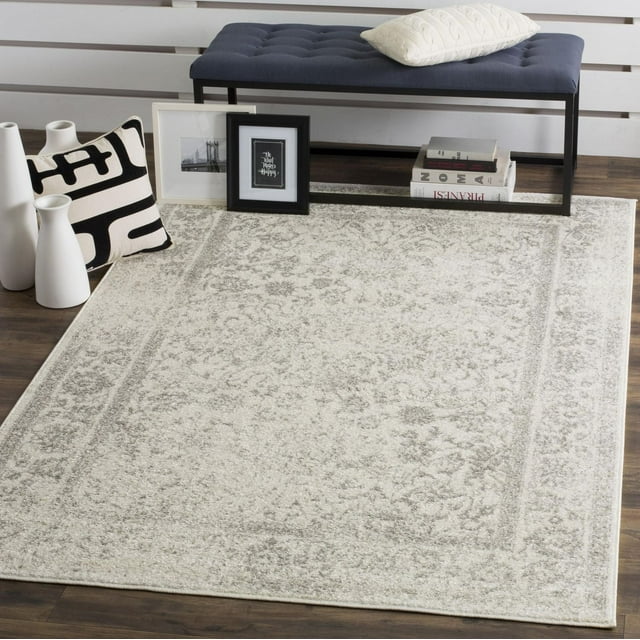 SAFAVIEH Adirondack Wyatt Traditional Area Rug in light gray and cream with subtle floral design, styled under a navy tufted bench on wood flooring.