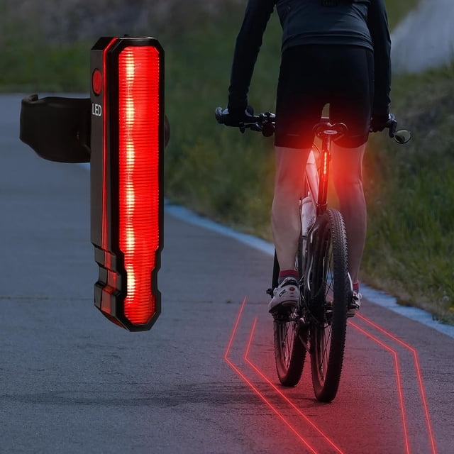 luz trasera de bicicleta recargable, luces traseras led rojas para bicicleta, 6 modos de luz, luz trasera láser para bicicleta, luz de advertencia de seguridad para ciclismo primer plano de una unidad rectangular negra con panel LED rojo y botón lateral; en uso muestra ciclista con la luz montada en la tija y líneas láser rojas proyectando un carril virtual sobre el pavimento; compacto y adecuada para transporte urbano.
