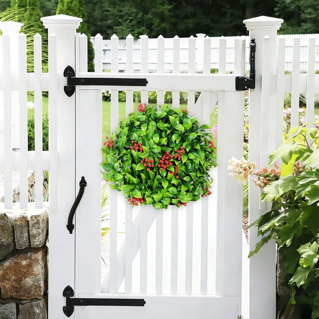 Plantas artificiales verdes con pequeñas bayas rojas y hojas verdes en un anillo decorativo.