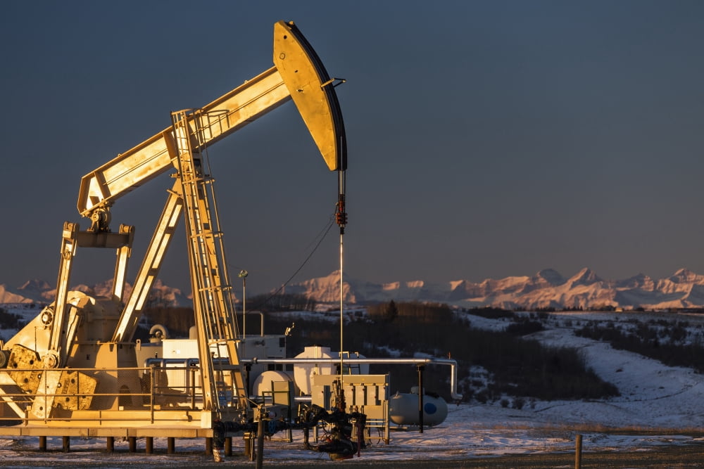 Two pump jacks at sunrise reflecting the warm morning light in a snow covered field and snow covered foothills and mountains in the background lit by the morning sun Alberta Canada Canvas Art - Michae