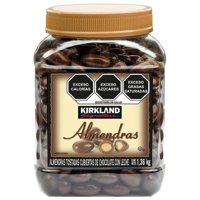 almendras cubiertas de chocolate con leche 1.36kg kirkland frasco frontal con almendras tostadas recubiertas de chocolate con leche, etiqueta beige con logo Kirkland Signature y sellos de advertencia nutricional, tapa roscada marrón; a menudo usadas como snack en reuniones o para bowls de convivencia.