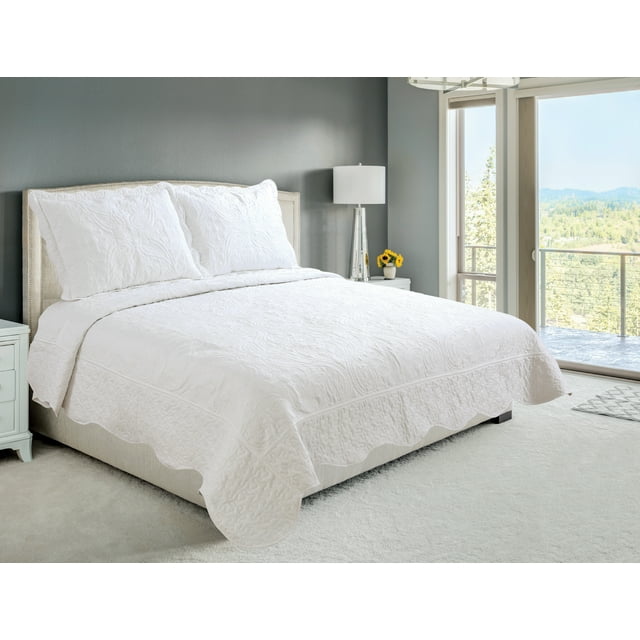 Ivory floral paisley pattern embroidered coverlet bedspread and quilted shams on king-size bed in modern bedroom with natural light.