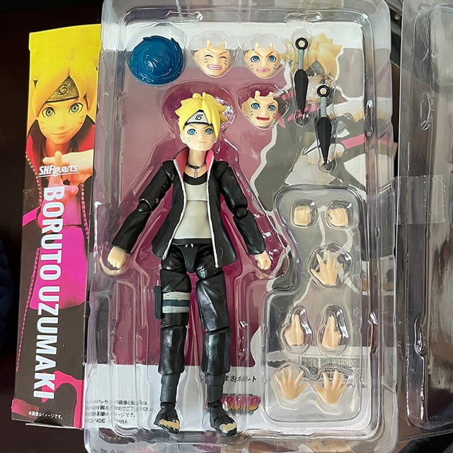 shfiguarts-figuras de acción de naruto, boruto, uzumaki, anime de las siguientes generaciones, uzumaki boruto, modelo shf, juguetes de regalo, muñeca — Figura articulada Uzumaki Boruto de ~15 cm en empaque blister, vista frontal; chaqueta negra con interior rosa, camiseta blanca, pantalones negros con banda gris en la pierna y cabello rubio; bandeja incluye manos intercambiables, dos shuriken, efecto de chakra azul y cabeza adicional, fondo con artwork vertical "BORUTO UZUMAKI". Su tamaño compacto lo hace adecuado como figura coleccionable o regalo para fans.