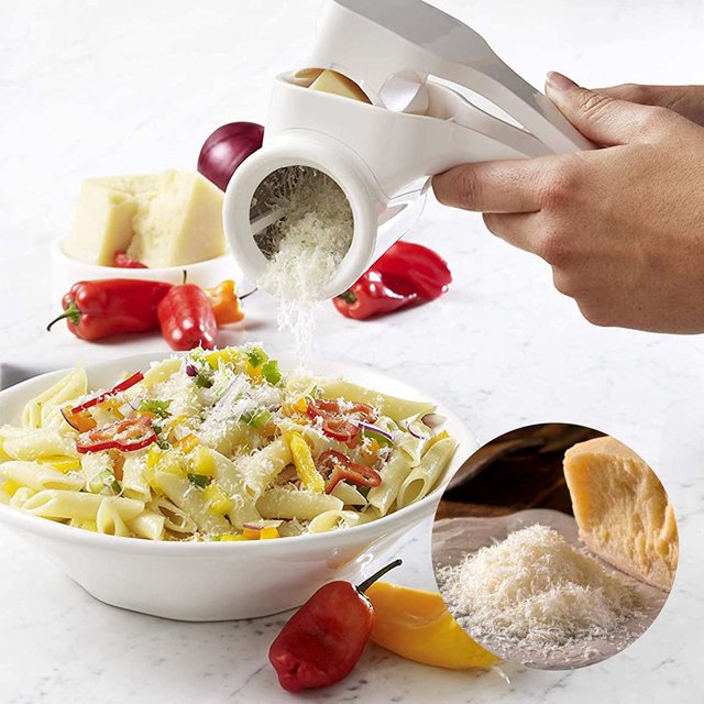 Multipurpose Rotary Cheese Grater Handheld Cheese Grinder For Parmesan Cheddar shown in use, grating cheese over a bowl of pasta. The white handheld grater features a rotary drum design with a crank handle. A close-up inset highlights grated cheese and a block of parmesan. Ideal for grating hard cheeses, nuts, and chocolate.