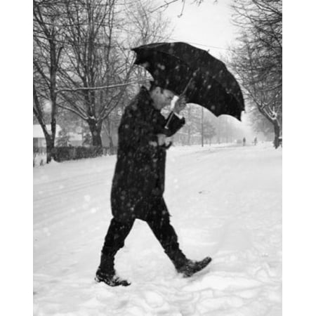 Mid adult man walking on snow covered road with umbrella Poster