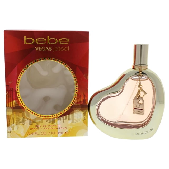 Perfume Bebe Vegas Dama EDP with a heart-shaped transparent bottle framed in gold-tone metal, featuring a small charm and gold cap, alongside its red and gold 'bebe VEGAS jetset' box containing 3.4 fl oz (100 ml) eau de parfum spray, offering floral notes of mango, jasmine, and musk, suitable as a stylish gift.