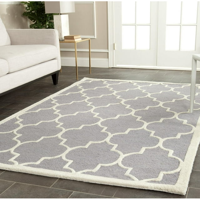 Safavieh Cambridge Kevin gray area rug with white geometric trellis pattern placed on dark tile floor next to beige sofa and gold side table.