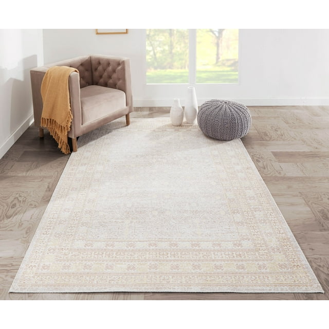 Traditional beige and cream patterned area rug on wooden floor in bright living space featuring taupe armchair with orange throw, gray knitted pouf, and white vases by window.