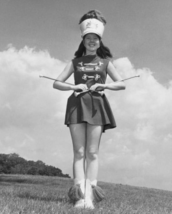 Drum majorette performing with two twirling batons and smiling Poster