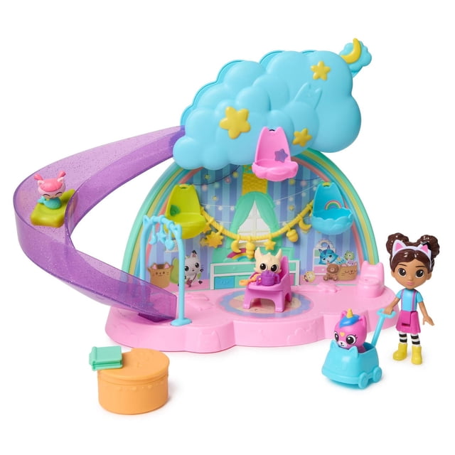 Gabby’s Dollhouse, Kitty Care Ear Purrfect Playroom, 17-piece playset with a pink base and purple glitter slide shaped like a cloud, three hanging chairs in pink, yellow, and blue, a 3-inch Gabby figure in blue top, pink skirt, and yellow boots, three baby kitties, high chair, bassinets, pushcart, and nursery accessories for imaginative dollhouse play.
