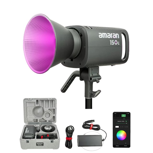 lámpara de vídeo aputure amaran 150v rgb 150w bowens mount vista 3/4 frontal con reflector Bowens instalado que emite luz rosa, cuerpo gris con el logo amaran 150c y asas traseras; montada en soporte, incluye funda EPP con adaptador y cables, y pantalla de control Sidus Link en teléfono; también adecuada como monolight para estudio.