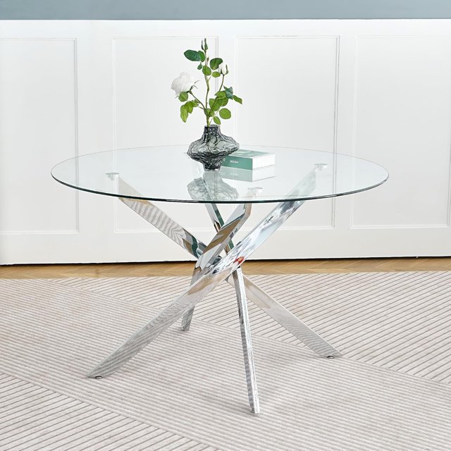 Heavenly Collection Star Dining Table with a 48-inch round clear tempered glass top featuring beveled edges and a polished chrome X-frame stainless steel base, displayed on a light striped rug with a black textured vase holding white roses and a design book on the tabletop, ideal for contemporary dining areas.