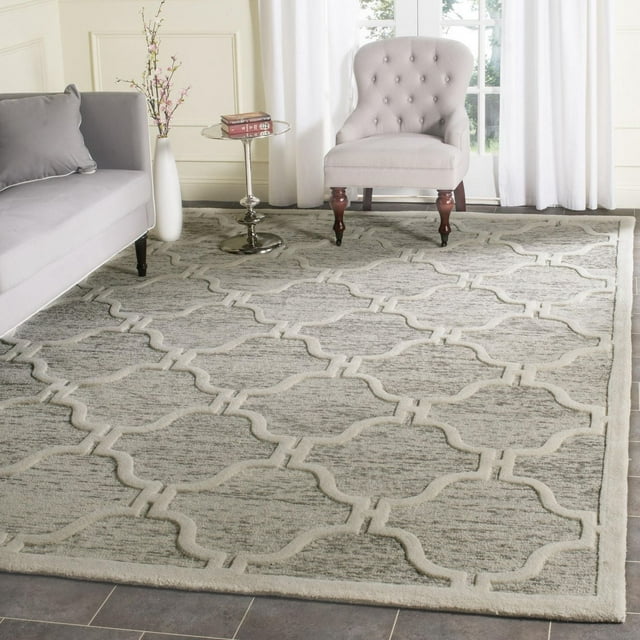 Safavieh Cambridge Kodey light gray area rug with faded geometric trellis pattern displayed in modern living room with gray sofa and white armchair.