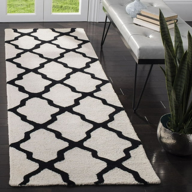 Safavieh Cambridge Liam black and white geometric area rug on dark hardwood floor beside gray bench with books and potted snake plant.