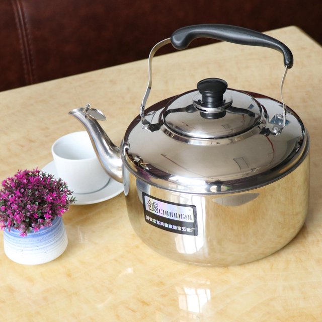 Kettle Stainless Steel Teapot for Boil Water/Coffee 6L with a polished stainless steel body, black PP grooved anti-slip handle, and a spout with a whistle feature. The teapot is placed on a light wood table alongside a white teacup and saucer, a small potted plant, and a brown background. Suitable for gas, electric, and induction stovetops, ideal for boiling water, making coffee, tea, or milk, and perfect for home, kitchen, camping, or travel.