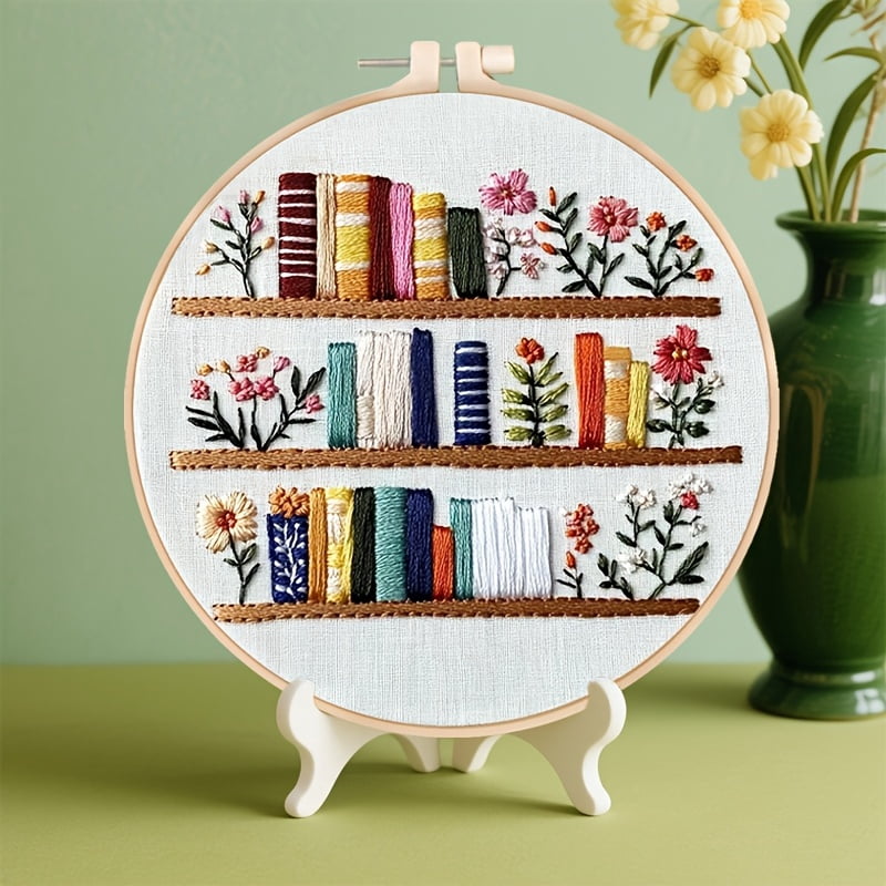 An Embroidery Kit Featuring a Bookshelf Floral Pattern Measuring, Suitable for Both Adults And Beginners. It Includes Instructions, Printed Fabric, an Embroidery Hoop, And Needle And Thread
