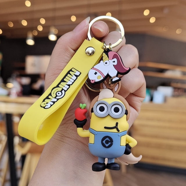 NAOJIE Minion Keychain with a yellow silicone strap featuring 'Minions' branding, a detailed Minion doll holding a red apple, and a unicorn charm attached to a durable metal ring. Ideal as a travel accessory or for decorating backpacks, wallets, or car keys.