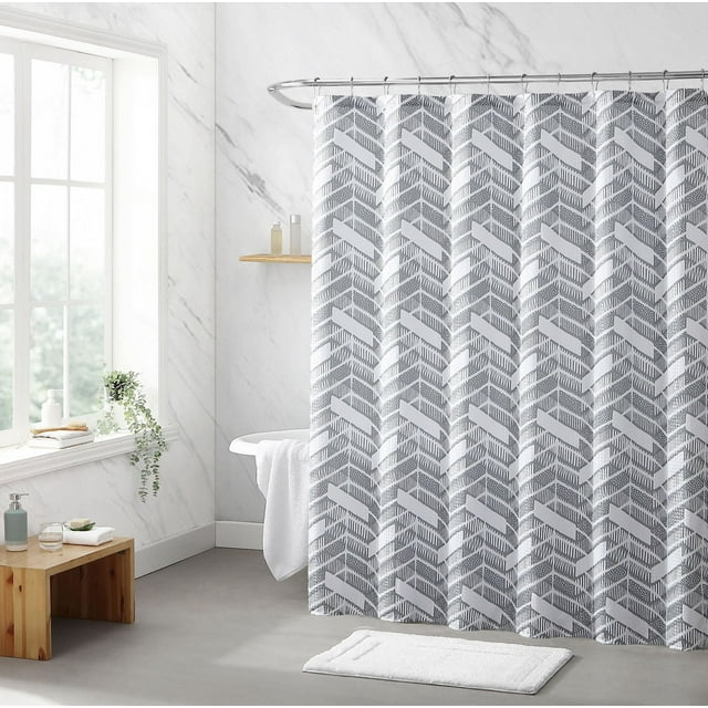 Gray and white chevron patterned fabric shower curtain hanging on a curved rod in a bright, modern bathroom with marble walls.