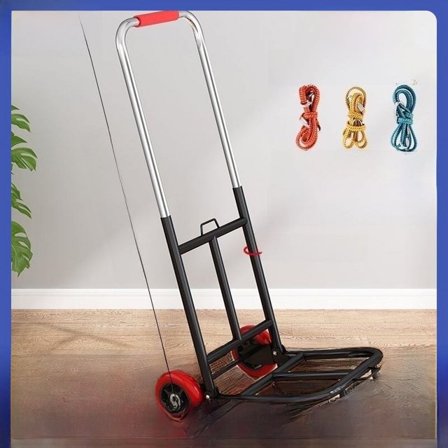 pequeño carrito plegable para el hogar, remolque para manipulación de compras, carrito de compras, carrito de equipaje portátil ligero con chasis negro y mango tubular metálico; vista 3/4 frontal que muestra plataforma plegable, empuñadura roja y sistema de cuatro ruedas con ruedas traseras rojas, diseño compacto y ligero para almacenamiento y uso manual en interiores y exteriores; a menudo usado para transportar comestibles o equipo de puestos.