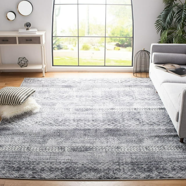 SAFAVIEH Amelia Manuel distressed southwestern area rug in gray and white tones displayed on hardwood floor next to a sofa, side table, and window.